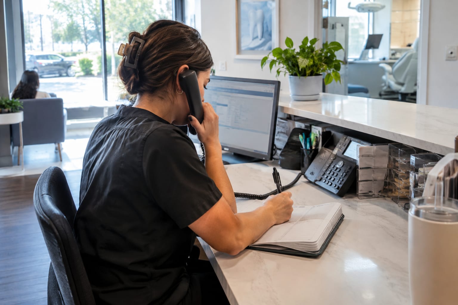 Dental receptionist on the phone writing in a call log notebook with lead source columns