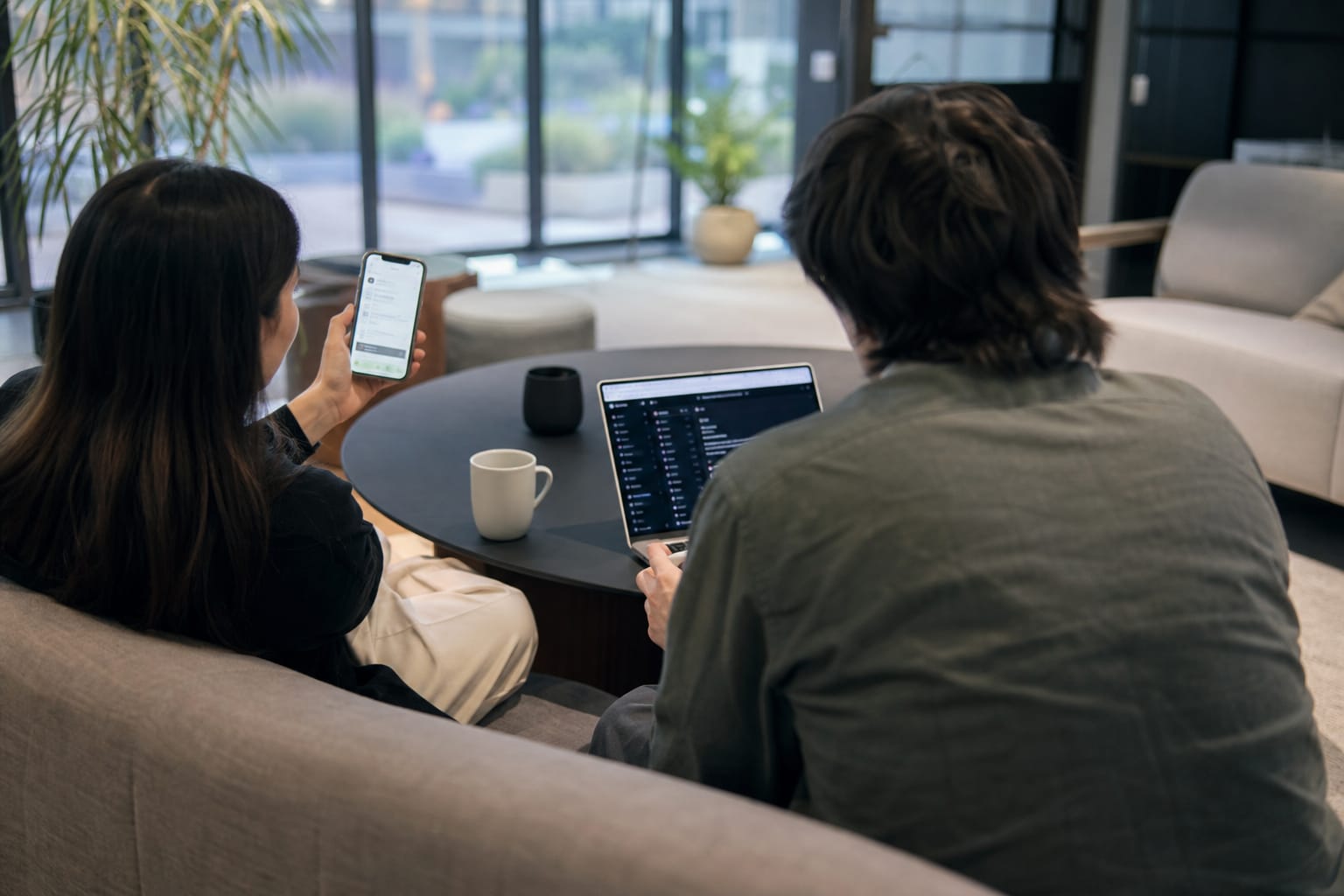 Two marketers on a sofa reviewing a phone showing an AI chat assistant answer that cites their product.