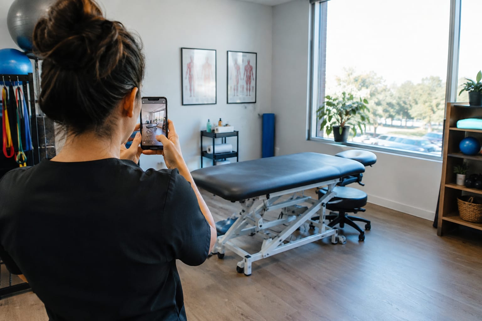 Physiotherapy clinic owner photographing a treatment room with a treatment table using a smartphone