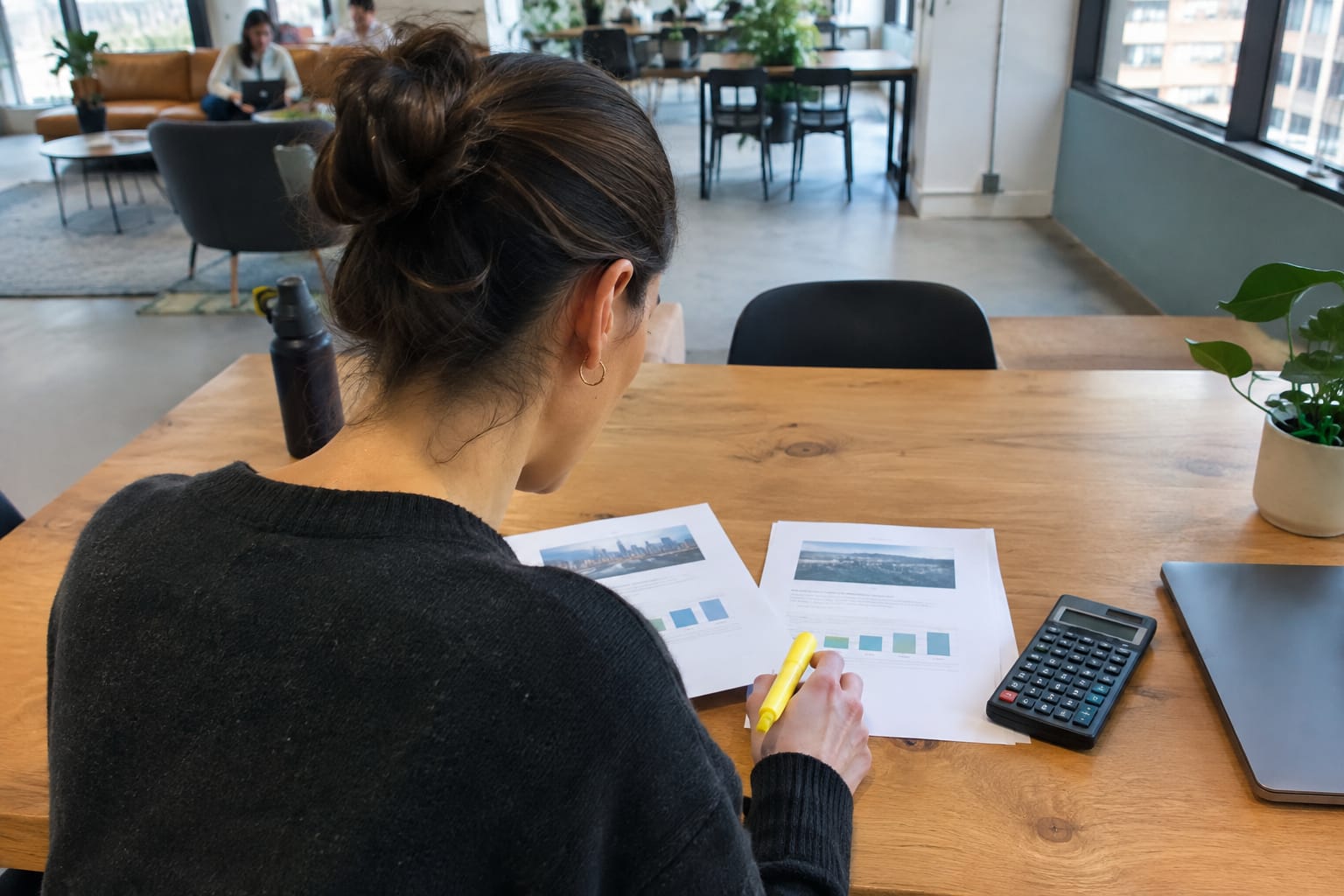 Marketing lead highlighting two printed proposals side by side on a table next to a calculator