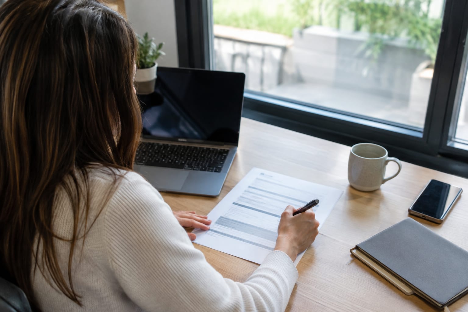 Accountant signing a printed page of service descriptions and prices with a pen beside an open laptop