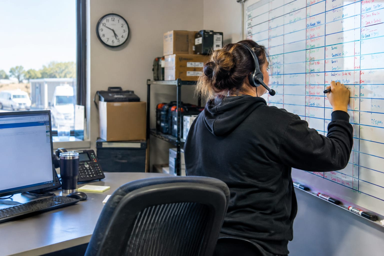Dispatcher in a headset writing on a paper schedule board crowded with handwritten HVAC appointments