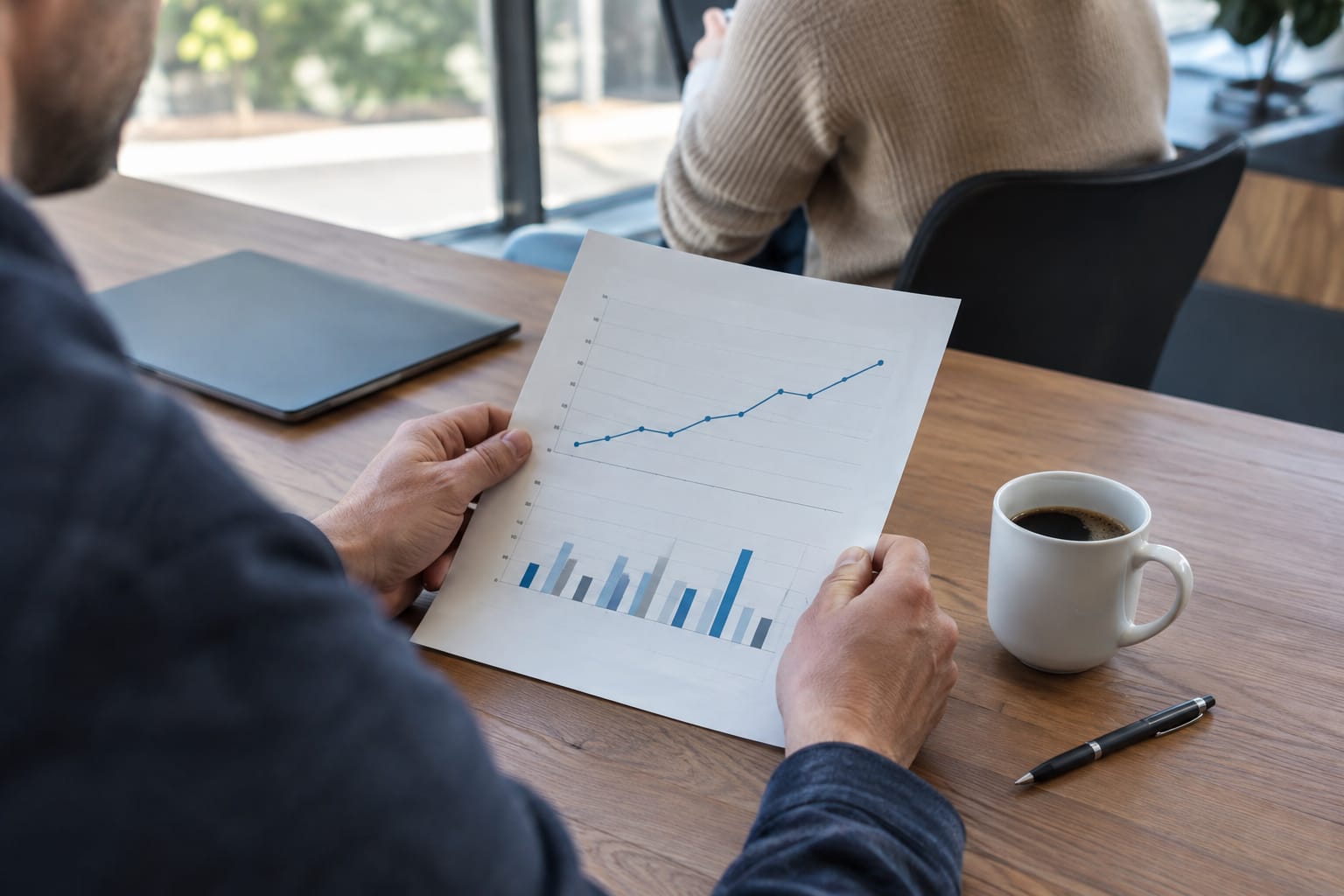 Hands holding a one-page printed results summary with a line chart beside a coffee cup and pen