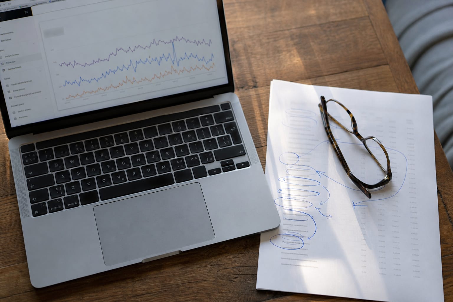 Laptop showing a Search Console graph beside a printed query report circled in blue pen and reading glasses.