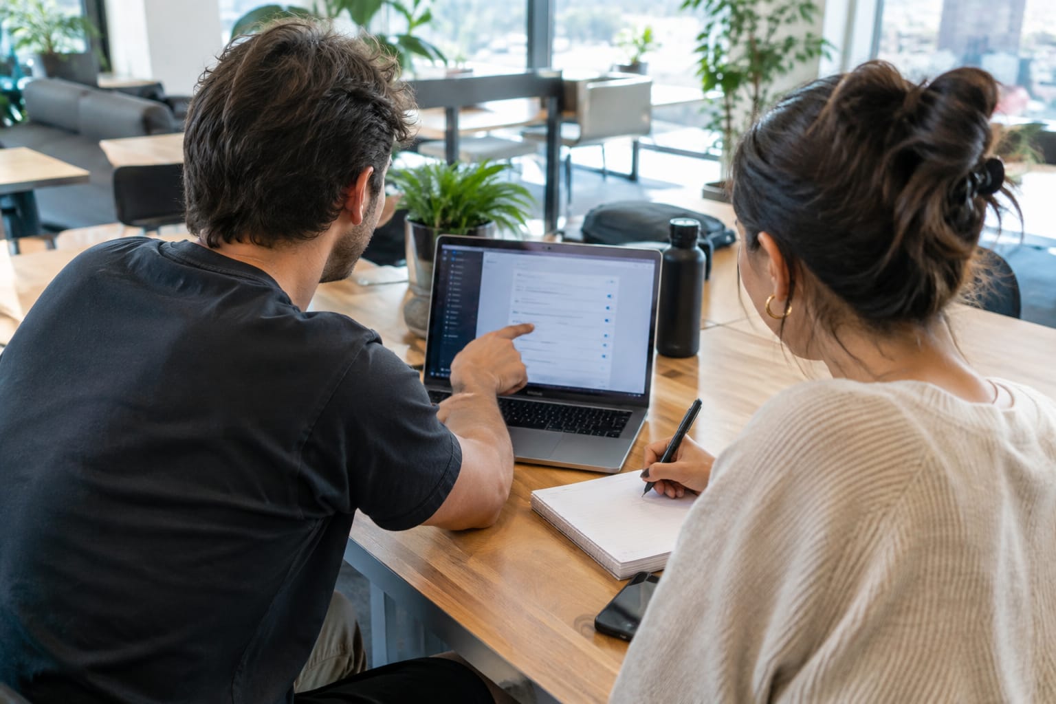 Developer pointing at a website settings panel on a laptop while a business owner takes notes
