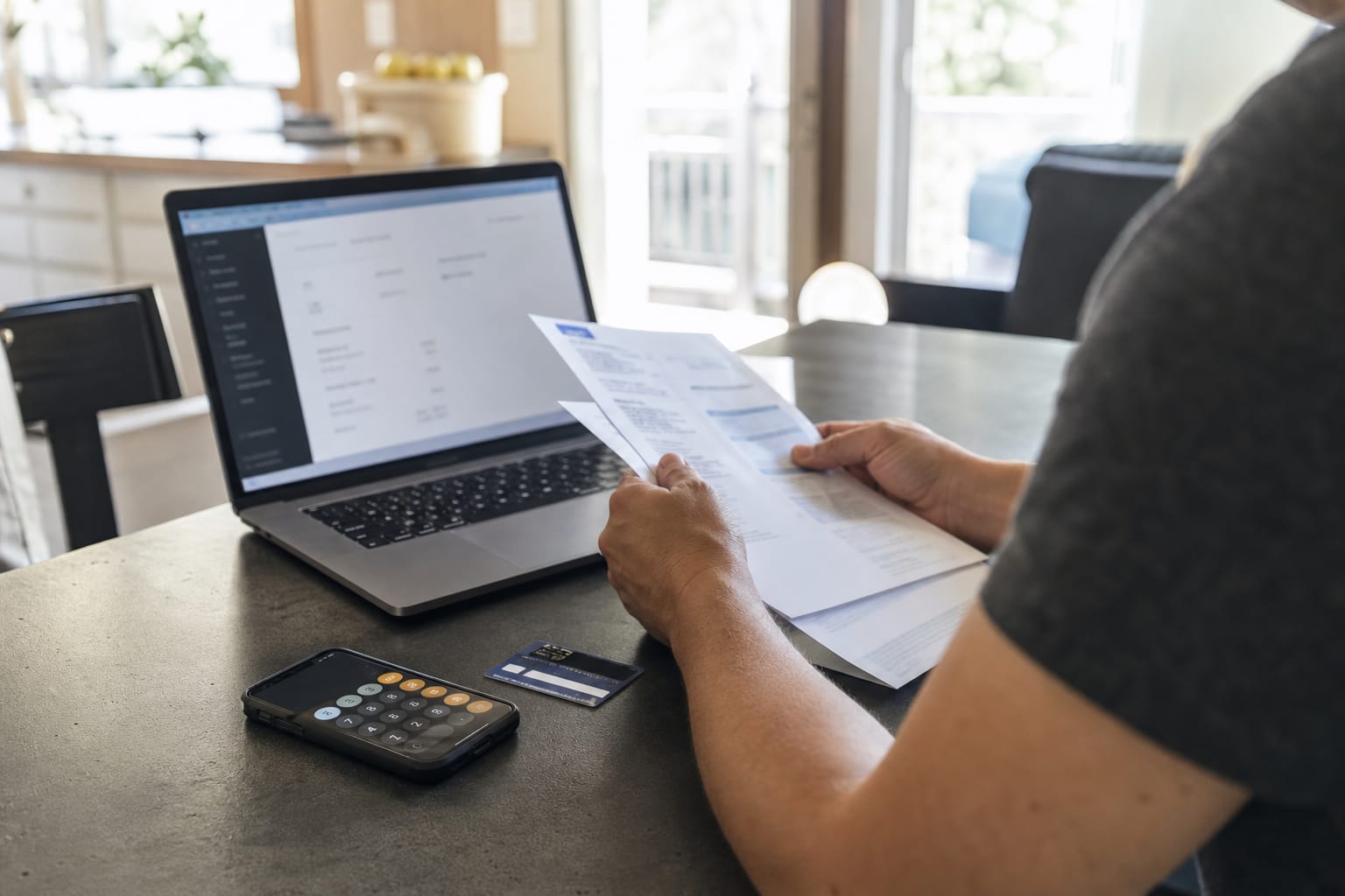 Invoice, credit card and phone calculator beside a laptop showing a billing settings screen