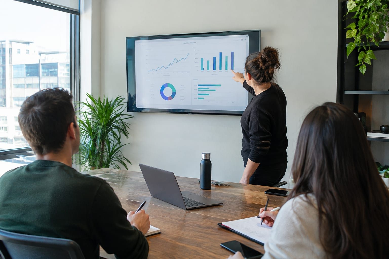 Agency owner pointing at a client report on a wall screen while two colleagues take notes