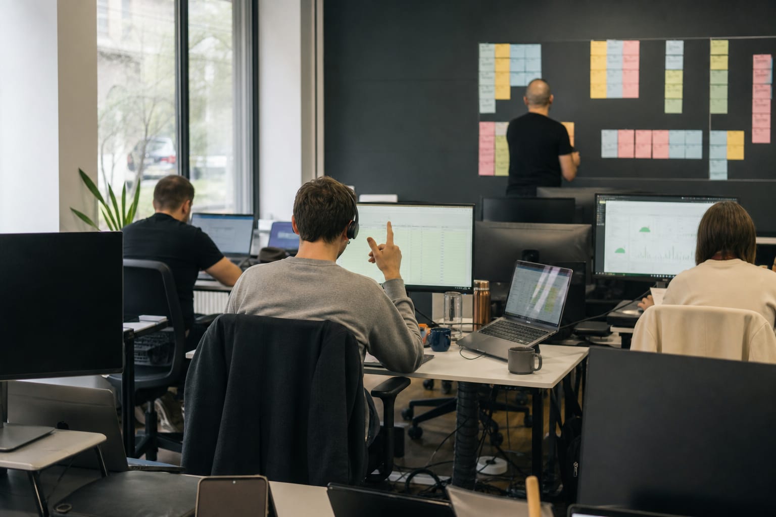 Agency team at desks with a wall board of coloured client account cards and someone on a headset call.